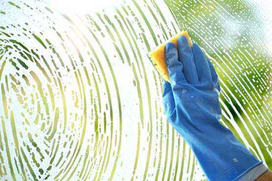 Rubber gloved hand cleaning window with sponge.