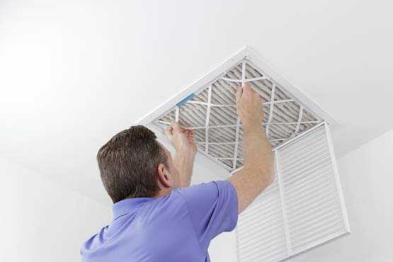 Caucasian male removing a square pleated dirty air filter with both hands from a ceiling air duct. Guy taking out an unclean air filter from a home ceiling air vent.