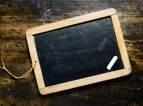 Small wooden framed chalkboard on a wooden table. Also, there is a piece of chalk. 