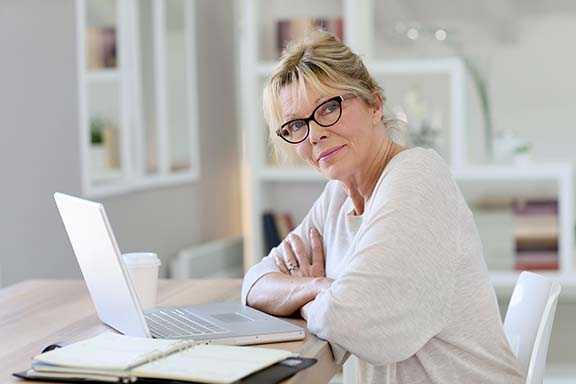 older woman sitting at desk in window looking happy