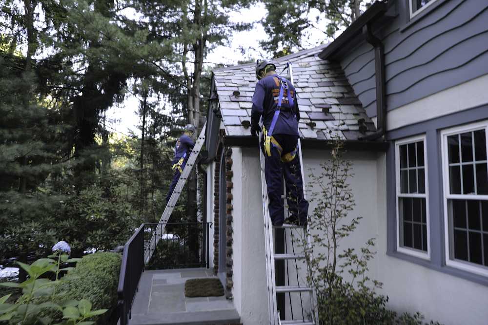 Man on top of latter cleaning gutters