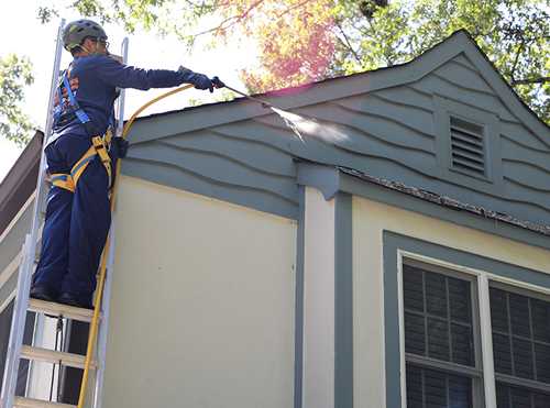 Technician power washing residential siding near the roofline.