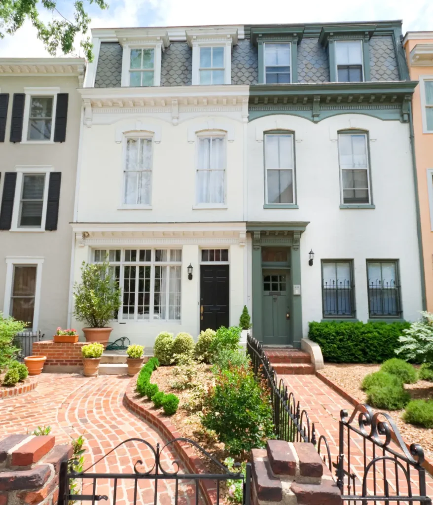 White three-story townhouse with decorative trim, tall windows, and a brick walkway garden leading to the front door.