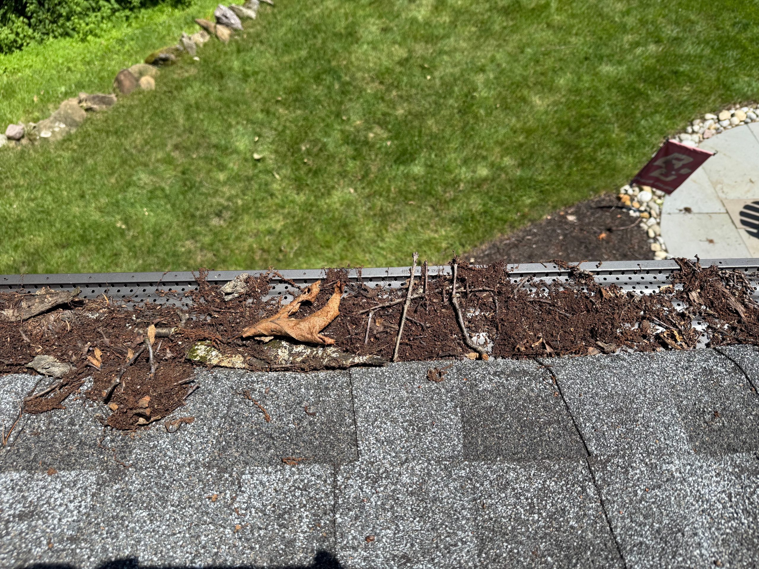 Overhead view of a gutter guard clogged with leaves, twigs, and organic debris on a residential roof.
