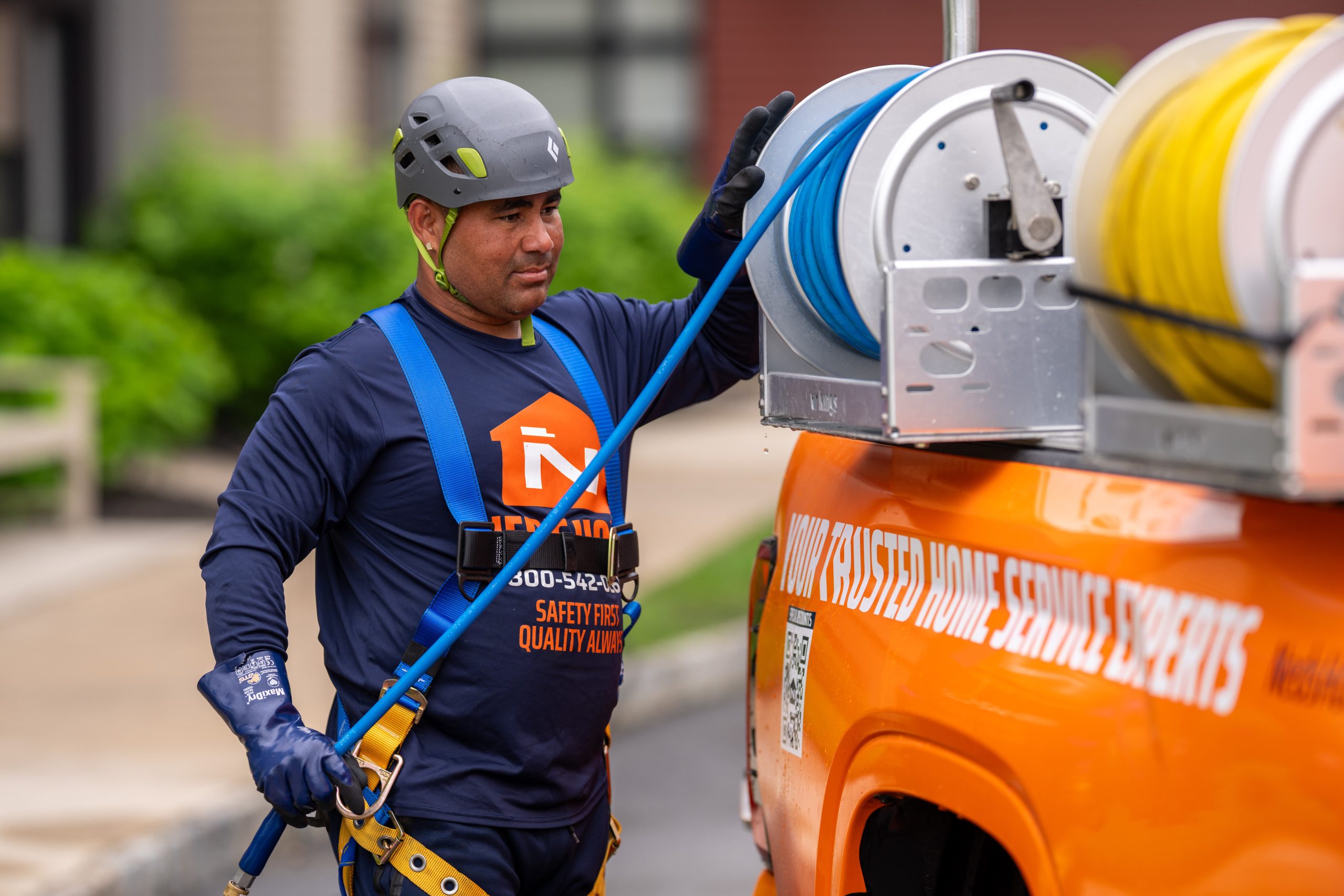 Ned's Home commercial services technician in safety harness and helmet preparing equipment at a branded service truck outside a commercial property.
