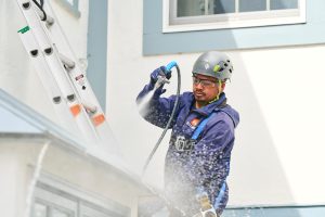 Technician performing power washing service on a home's exterior.