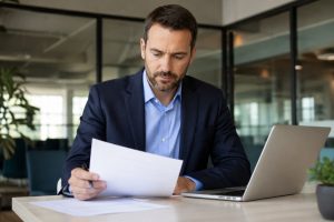 Property manager reviewing vendor documents at a desk with a laptop open.