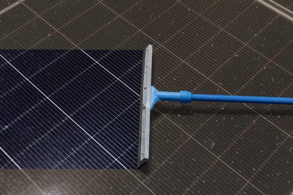 Squeegee tool cleaning dust and debris off a solar panel