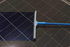 Squeegee tool cleaning dust and debris off a solar panel