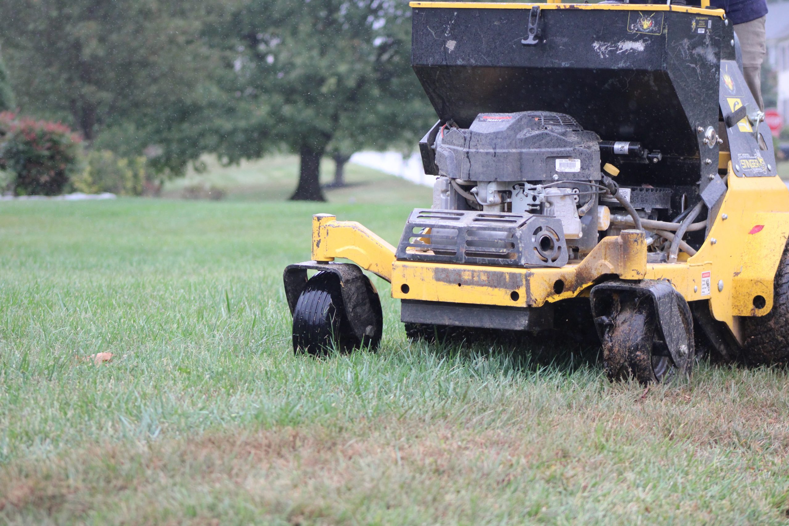 Professional broadcast spreader applying lawn treatment across a residential yard, used for services like lime application and fertilization.